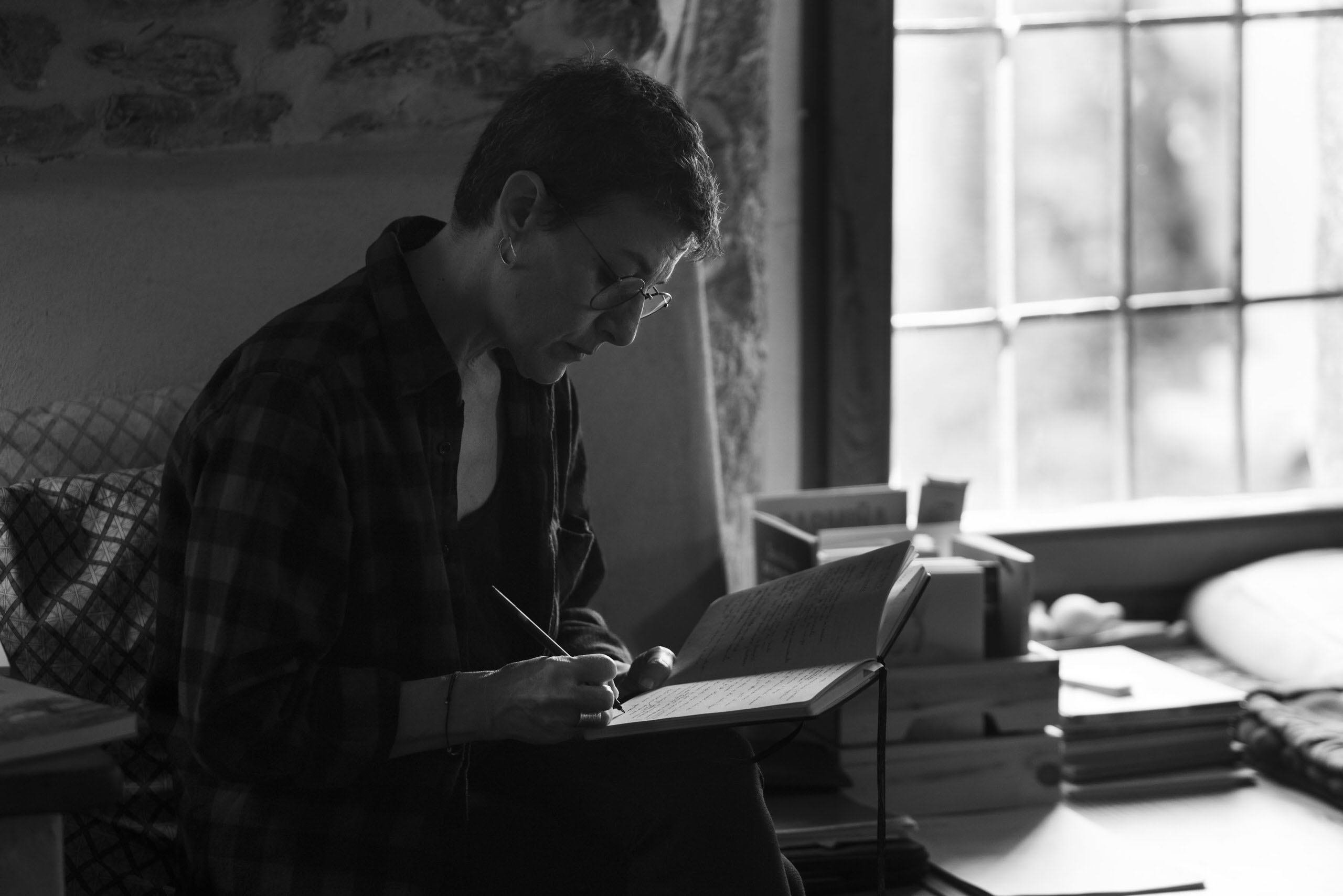Persona escribiendo en cuaderno junto a una ventana en un espacio íntimo