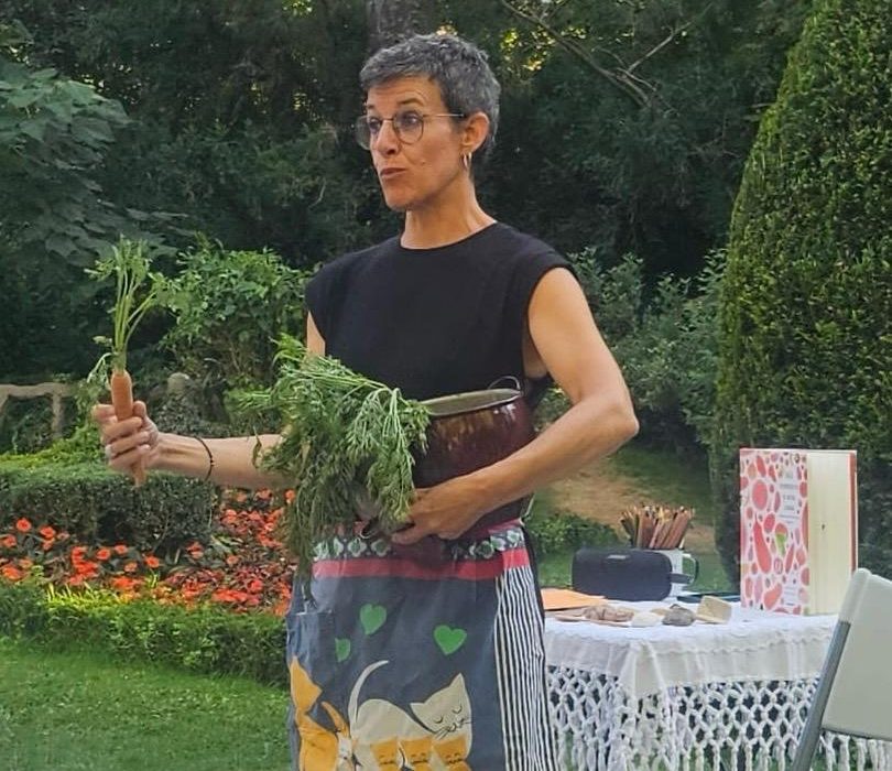 Diana Sanchís Lobato durante una actividad de narración y lectura al aire libre, con un libro ilustrado y una zanahoria en la mano.