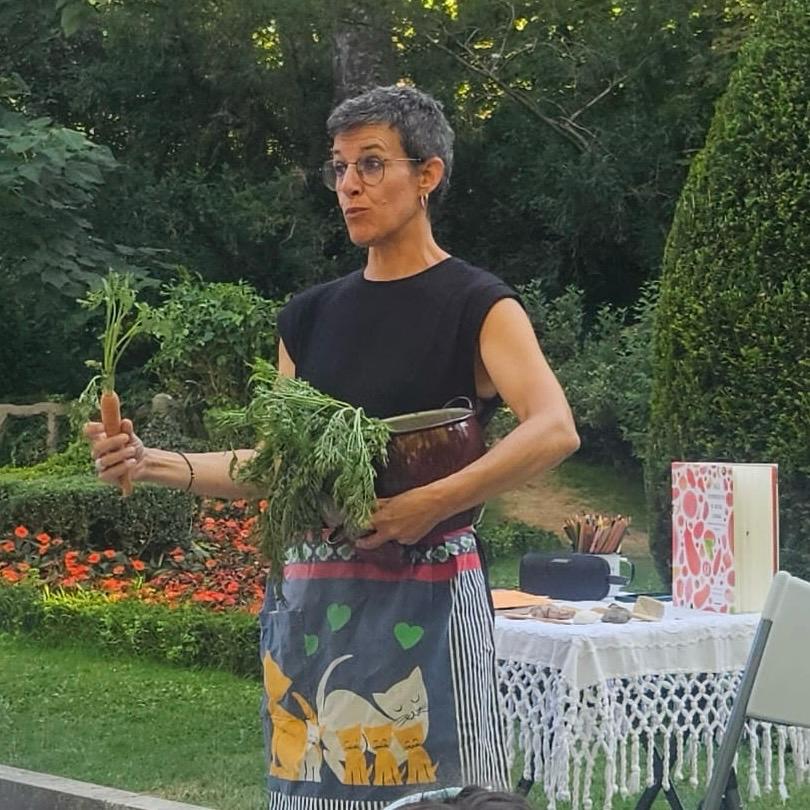 Diana Sanchís Lobato durante una actividad de narración y lectura al aire libre, con un libro ilustrado y una zanahoria en la mano.